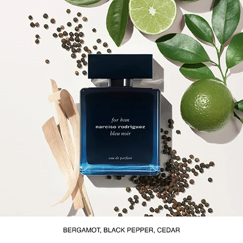 A blue perfume bottle labeled for him, narciso rodriguez bleu noir, with green lime slices, green leaves, and scattered black peppercorns, accompanied by the text bergamot, black pepper, cedar.