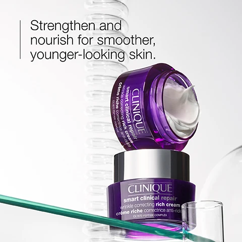 Image 1 - Two jars of Clinique skincare products, one partially open, with a smooth cream visible inside, accompanied by the text Strengthen and nourish for smoother, younger-looking skin. and smart clinical repair wrinkle correcting rich cream.
Image 2 - Image shows three round containers with skincare ingredients: a container with a beige powder labeled Peptides, a container with a clear gel labeled Soybean seed extract, and a container with a viscous liquid labeled Hyaluronic acid, along with brief descriptions of each ingredients benefits.
Image 3 - A creamy, white substance is spread across the surface with icons representing three actions: a weight for strengthen, a wavy line for smooth, and a droplet for hydrate.
Image 4 - A light purple background displays a table with two check marks indicating that the product is free of fragrance and oil.