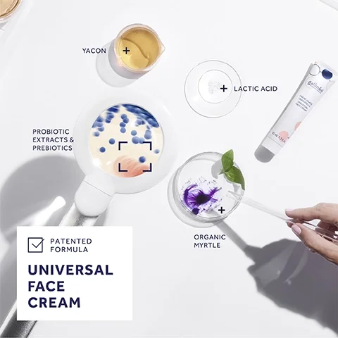 An overhead view of a tabletop scene featuring a hand using a pipette, various ingredients in small containers including yacon, probiotic extracts and prebiotics, a white powder labeled lactic acid, and organic myrtle, alongside a tube of face cream with the text patented formula and universal face cream.